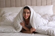 © New Africa - Cheerful young woman covered with warm white blanket lying in bed