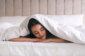 Wall Mural - Young woman covered with warm white blanket sleeping in bed