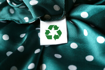 Clothing label with recycling symbol on green garment, closeup