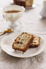 Wall Mural - Slice of Pound Loaf Cake with raisins on white porcelain plate and cup of tea on greige linen tablecloth. Selective focus
