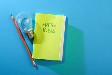 Sticker - Directly Above Shot Of Note Pad with text fresh ideas and light bulb On blue Background