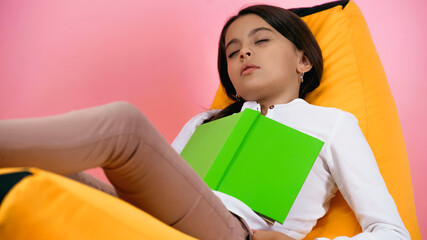 child sleeping with book on bean bag chair on pink