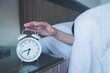 © photobuay - Close up of man lying in bed turning off hand reaching out for alarm clock color black Wake up late at morning.