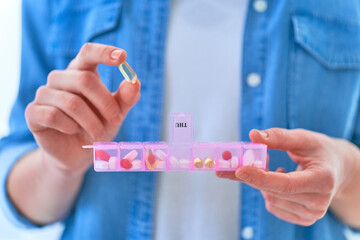 Wall Mural - Close up female hands holding pill box. Woman taking medicine and omega 3 dietary supplement for health. Fish oil softgel, vitamin D and C. Weekly dosage of medication in pill dispenser