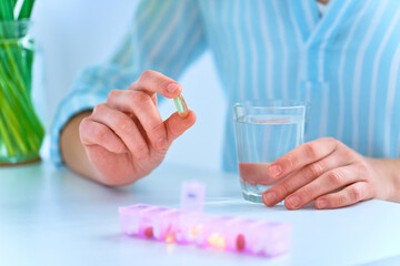 Wall Mural - Woman taking medicine and omega 3 dietary supplement to health from pill box. Weekly dosage of medication in pill dispenser