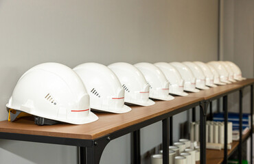 White protective engineering helmets lie in a row on a shelf in a factory, Industrial safety and labor protection