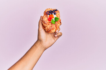 Wall Mural - Hand of hispanic man holding sweet bun over isolated pink background.