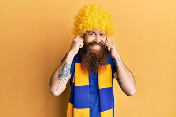 Canvas Print - Redhead man with long beard football hooligan cheering game wearing funny wig covering ears with fingers with annoyed expression for the noise of loud music. deaf concept.