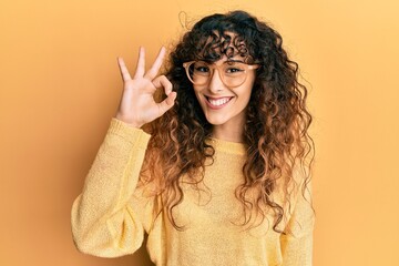 Young hispanic girl wearing casual clothes and glasses doing ok sign with fingers, smiling friendly gesturing excellent symbol