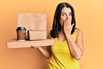 Canvas Print - Middle age brunette woman holding take away food covering mouth with hand, shocked and afraid for mistake. surprised expression