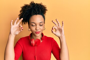 Sticker - Young african american girl listening to music using headphones relax and smiling with eyes closed doing meditation gesture with fingers. yoga concept.