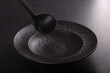Trendy design kitchen accessories, black plate and ladle on dark background.