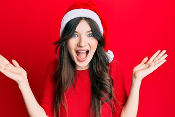 Wall Mural - Young beautiful caucasian girl wearing christmas hat celebrating victory with happy smile and winner expression with raised hands