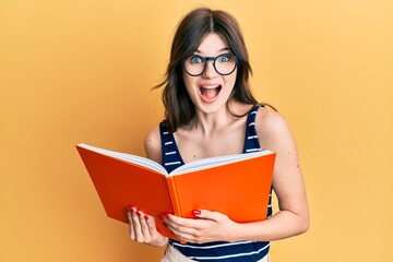 Poster - Young beautiful caucasian girl reading a book wearing glasses celebrating crazy and amazed for success with open eyes screaming excited.