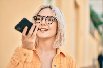 Sticker - Young blonde girl smiling happy sending voice message using smartphone at the city.