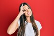 © Krakenimages.com - Young brunette woman wearing casual white tshirt over red background doing ok gesture with hand smiling, eye looking through fingers with happy face.