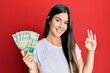 © Krakenimages.com - Young brunette woman holding hong kong 50 dollars banknotes doing ok sign with fingers, smiling friendly gesturing excellent symbol