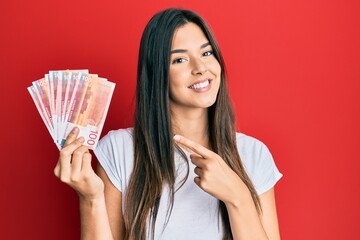 Poster - Young brunette woman holding 100 norwegian krone banknotes smiling happy pointing with hand and finger