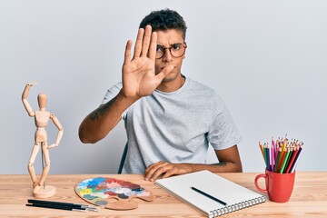 Poster - Young handsome african american man painter sitting palette and art manikin doing stop sing with palm of the hand. warning expression with negative and serious gesture on the face.