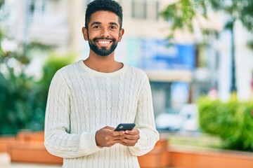 Poster - Young african american man smiling happy using smartphone at the park.