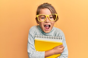 Wall Mural - Little beautiful girl wearing glasses and holding books smiling and laughing hard out loud because funny crazy joke.