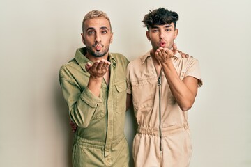 Poster - Homosexual gay couple standing together wearing casual jumpsuit looking at the camera blowing a kiss with hand on air being lovely and sexy. love expression.