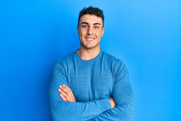 Hispanic young man wearing casual winter sweater happy face smiling with crossed arms looking at the camera. positive person.