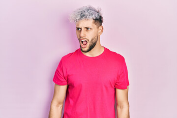 Young hispanic man with modern dyed hair wearing casual pink t shirt angry and mad screaming frustrated and furious, shouting with anger. rage and aggressive concept.