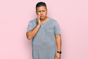 Young latin man wearing casual clothes touching mouth with hand with painful expression because of toothache or dental illness on teeth. dentist