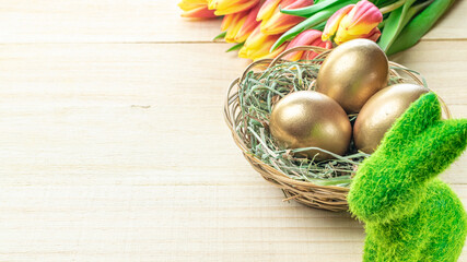 Wall Mural - Easter egg. Happy Easter decoration: Golden eggs in basket with spring tulips, white feathers on wooden background. Traditional decoration in sun light.