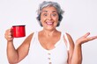 Senior hispanic woman holding coffee celebrating achievement with happy smile and winner expression with raised hand