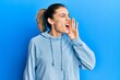 © Krakenimages.com - Young caucasian blonde woman wearing casual sweatshirt shouting and screaming loud to side with hand on mouth. communication concept.