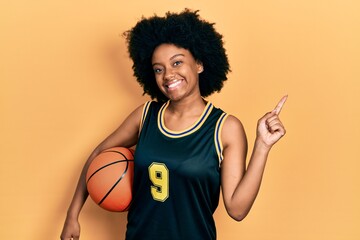 Poster - Young african american woman holding basketball ball smiling happy pointing with hand and finger to the side