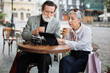 © sofiko14 - Mature man and woman in stylish outfits using digital tablet while drinking coffee on cafe terrace. Happy senior couple relaxing outdoors with modern technology.