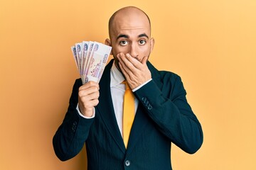 Wall Mural - Young hispanic business man holding russian 500 ruble banknotes covering mouth with hand, shocked and afraid for mistake. surprised expression