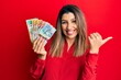 © Krakenimages.com - Beautiful brunette woman holding australian dollars pointing to the back behind with hand and thumbs up, smiling confident