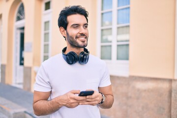 Wall Mural - Young hispanic man smiling happy using smartphone and headphones at city.