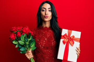 Wall Mural - Beautiful hispanic woman holding anniversary gift and roses bouquet looking at the camera blowing a kiss being lovely and sexy. love expression.