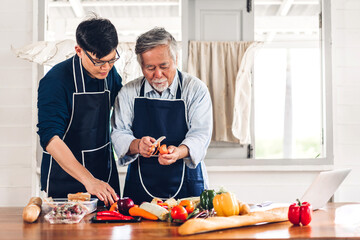 Portrait of happy love asian family senior mature father and young man adult son having fun cooking food together and look for recipe on Internet with laptop computer to prepare the yummy eating lunch