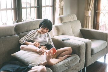 Wall Mural - Young adult asian lover couple sitting on sofa cozy style indoor on day.