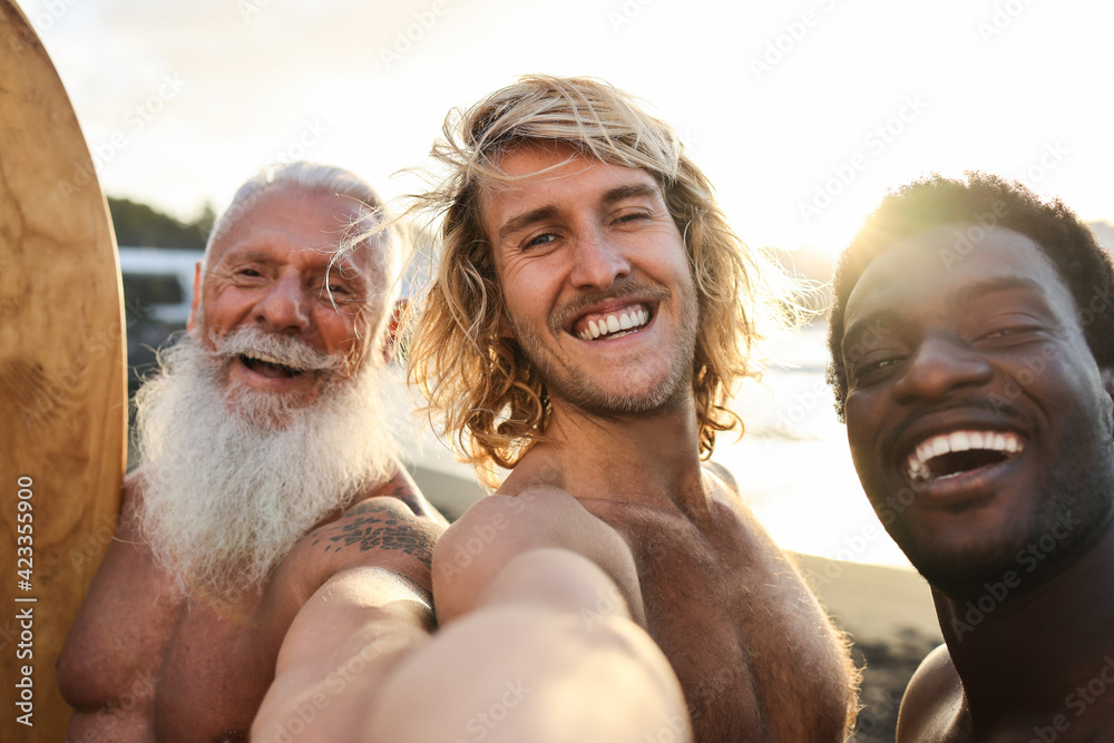 Multi generational surfer friends having fun on the beach after surf session - Multiracial friendship and extreme sport lifestyle concept - Main focus on center guy face - obrazy, fototapety, plakaty 