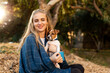 © Алина Битта - Nice laughing blonde girl in holding little dog jack russel and cup in hands. happily spending time on picnic in park covered blue blanket on sunset autumn forest background