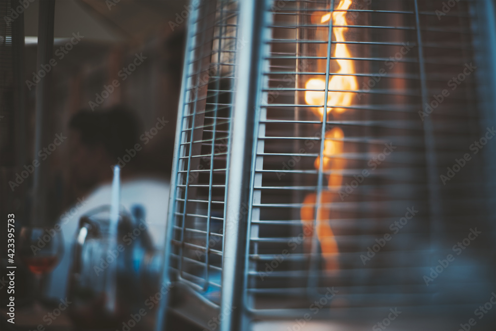 A true tilt-shift photo of a street gas heater for a patio with a flame of fire inside, with a selective focus on the part of a protective metal grid - obrazy, fototapety, plakaty 