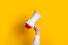 Female Hand Holds A White With A Red Megaphone On A Yellow Background.