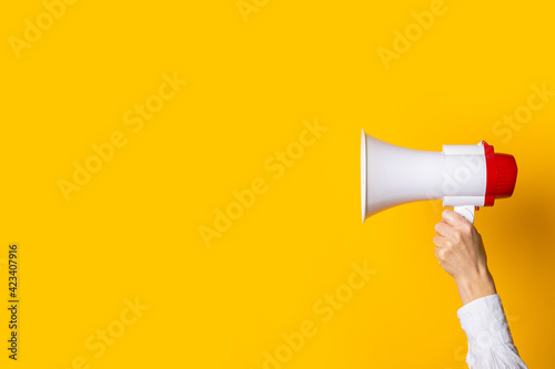 Obraz Dibond female hand holds a white with a red megaphone on a yellow background.