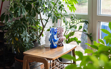 Mid-century blue and red striped modern artisan glass vase collection on a wooden table with plants before the window