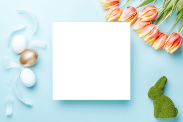 Wall Mural - Easter holiday. Golden, white colour egg in basket with spring tulips, feathers on pastel blue background in Happy Easter decoration. Spring holiday top view with copy space.