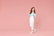 Full length body of young student positive smiling happy caucasian redhead woman 20s wearing blue shirt pants walking going looking back aside isolated on pastel pink color background studio portrait.