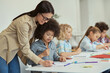 © Kostiantyn - Helpful young female teacher showing how to do task to little schoolboy. Kids sitting at the table, studying in elementary school classroom