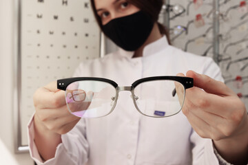 Canvas Print - Young caucasian woman optometrist shows glasses for vision into the camera. Selection of correction for the eyes. Stylish retro eyeglass frame